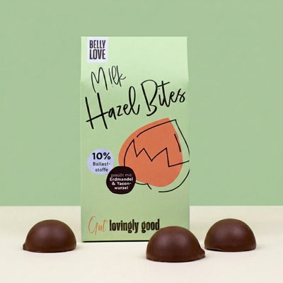 Belly Love Milk Hazel Bites Verpackung mit dunklen Schokoladenpralinés davor – bio, industriezuckerfrei, 10% Ballaststoffe