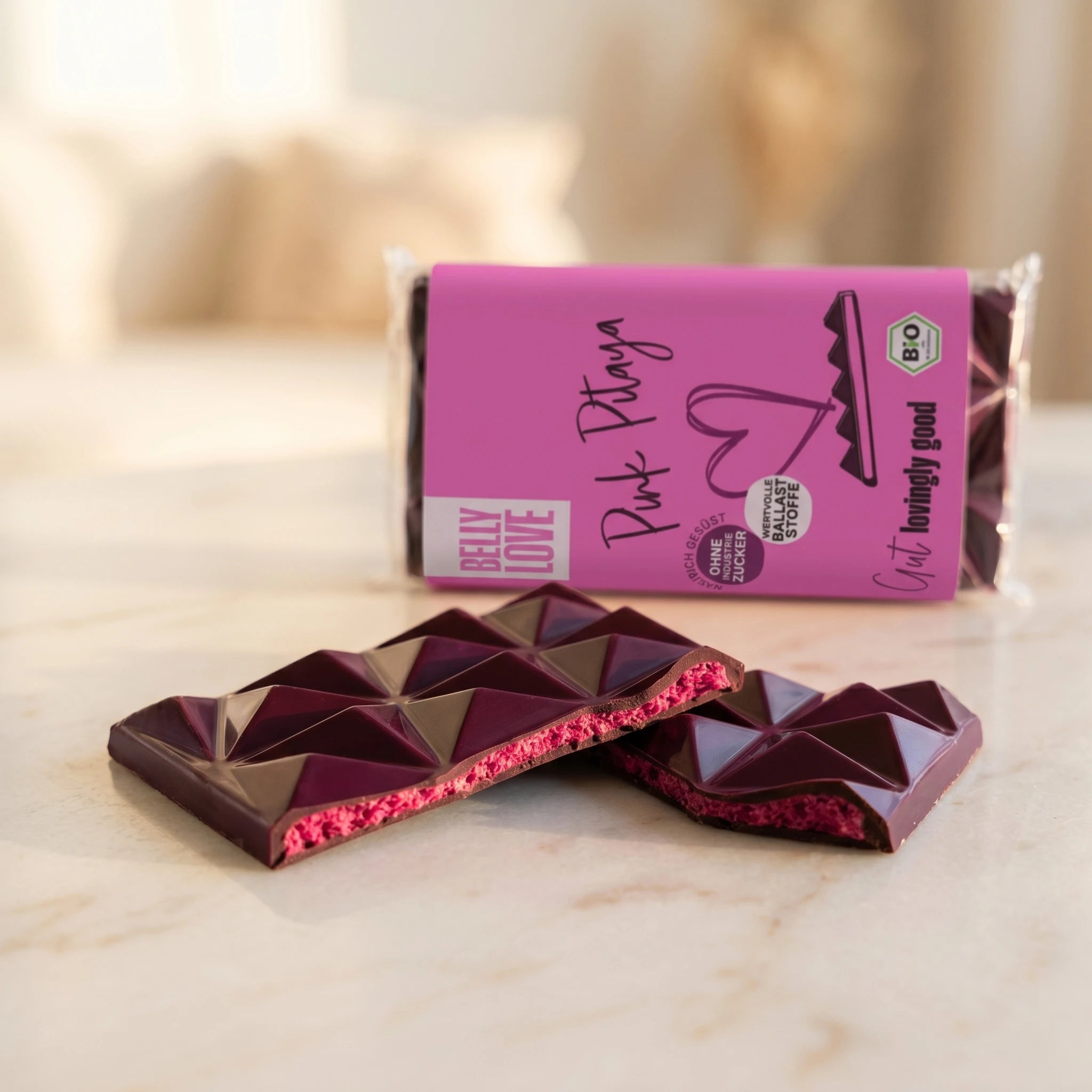 Belly Love Pink Pitaya Tafel Lifestyle – Schokoladenstücke auf Marmor, pinke Füllung