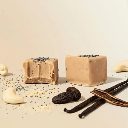 Zwei Tonka Mohn Pralinen von Belly Love in Nahaufnahme – zuckerfrei, clean label und reich an Ballaststoffen, gesüßt mit Erdmandel, Yaconwurzel und Datteln, verfeinert mit Vanille und Mohn, umhüllt von unserer blonden Schokolade (wie weiße Schokolade). Vegan, ohne glutenhaltige Zutaten und biozertifiziert.